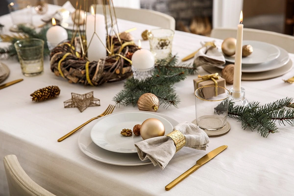 Table dresses for Christmas dinner with light tablecloth and plates, candles and gold cutlery