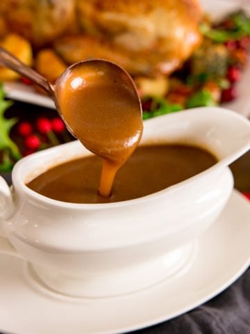 Christmas gravy being poured off a spoon into a white gravy boat