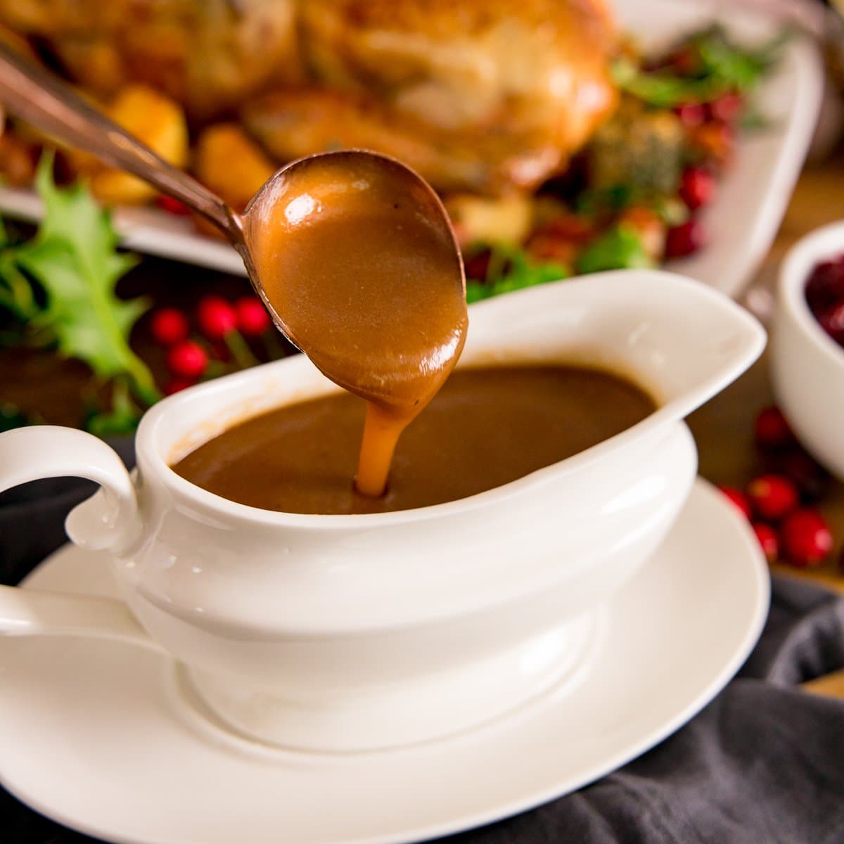 Christmas gravy being poured off a spoon into a white gravy boat
