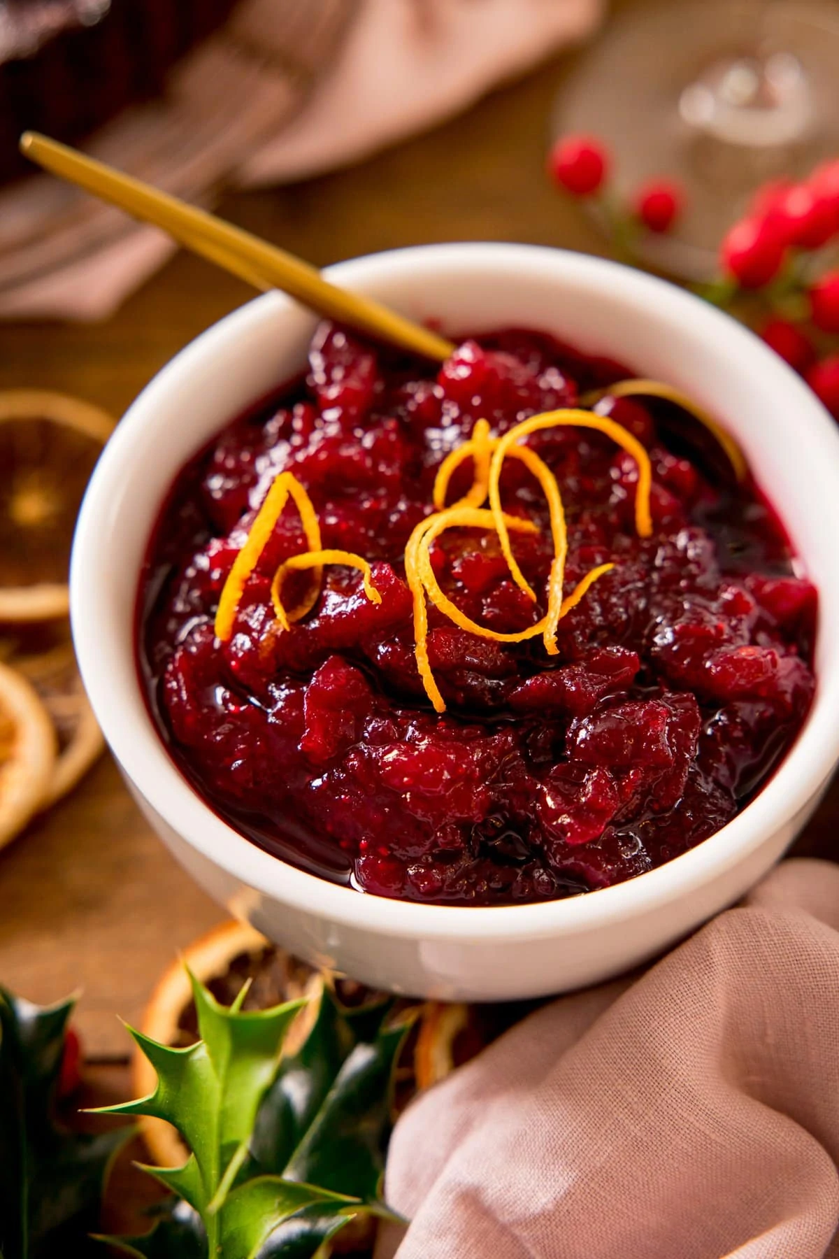 Cranberry sauce topped with orange zest in a white bowl. Festive decorations scattered around.