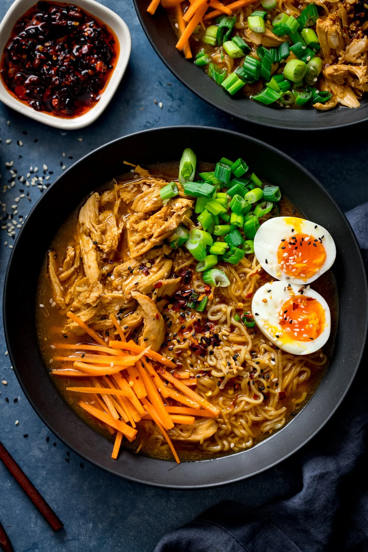 Overhead of chicken ramen in a black bowl with toppings of egg, spring onions and carrot strips.