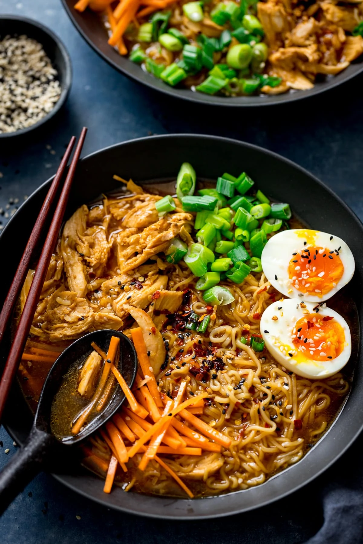 Chicken Ramen in a black bowl topped with egg, carrots and spring onions. Spoonful being taken.