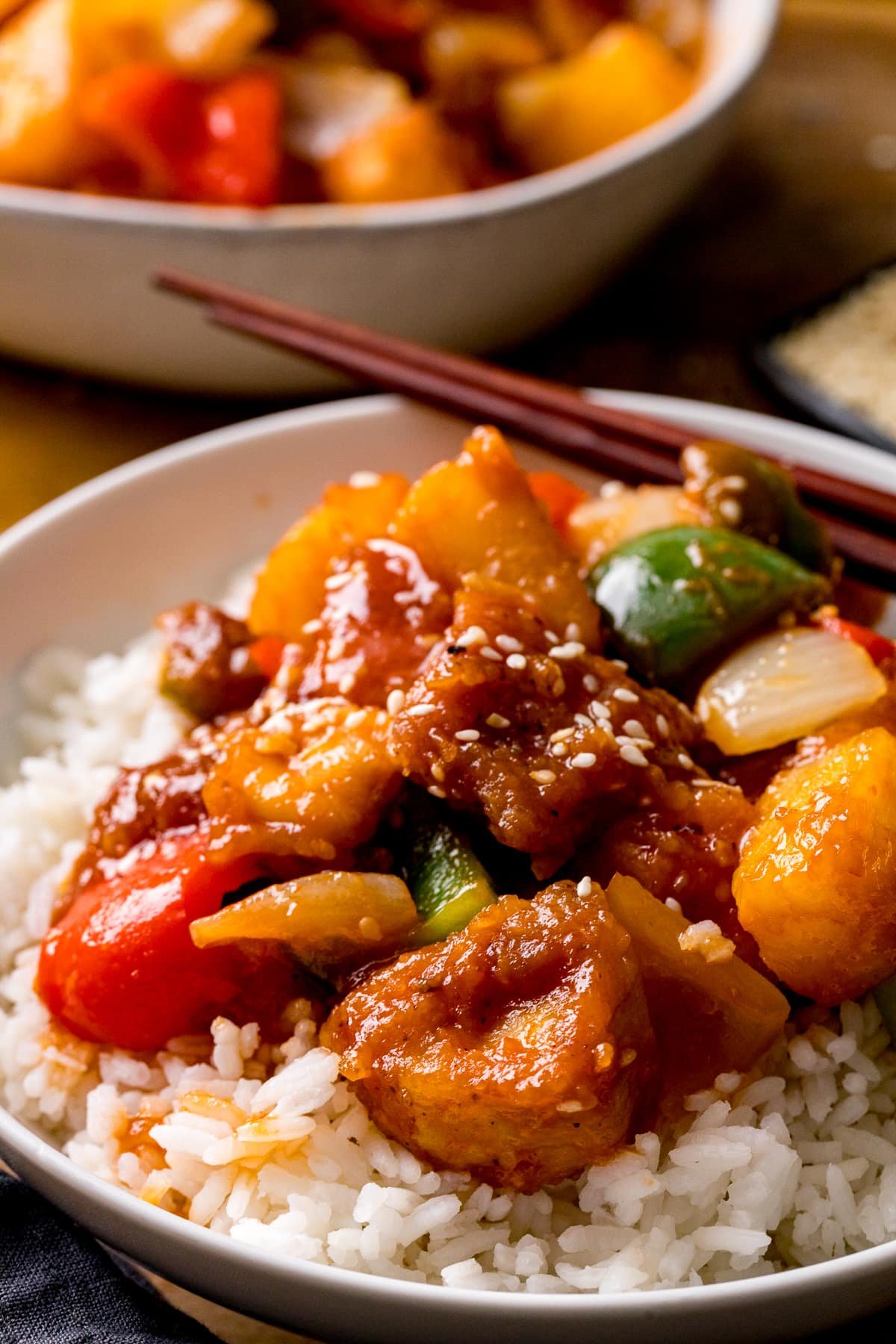 Sweet and sour turkey on top of boiled rice in a white bowl. Further bowl in the background.