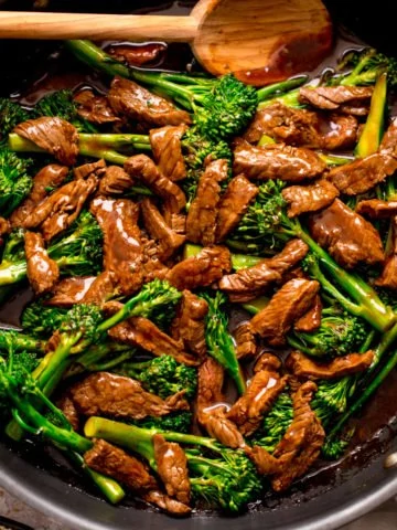 beef and broccoli stir fry in a pan with a wooden spoon