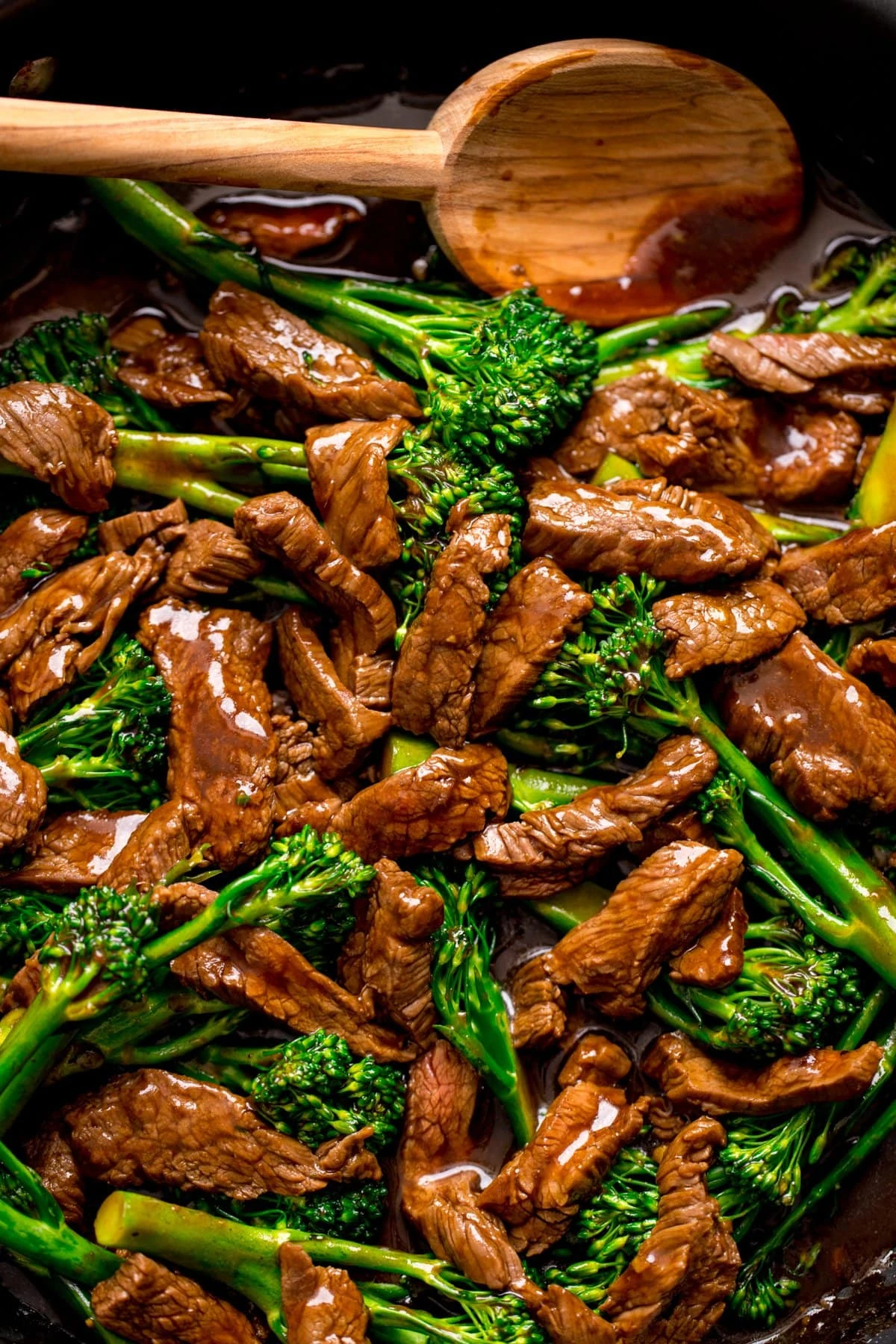 Close up overhead image of Chinese beef and broccoli in a pan with a wooden spoon.