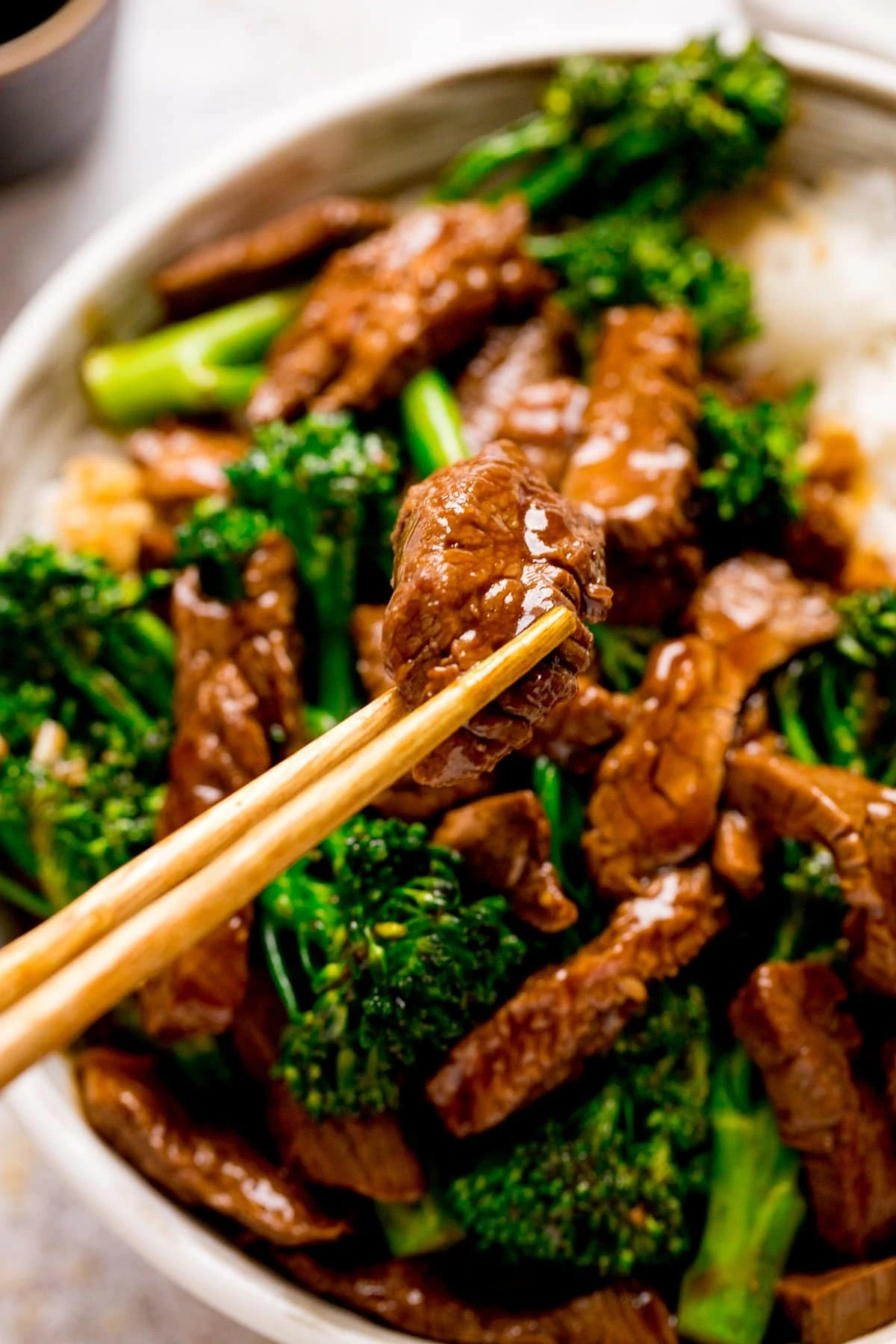 Chopsticks taking a piece of Chinese beef from a bowl of beef and broccoli.