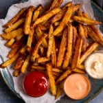 Chips on a plate on top of baking parchment. 3 dipping bowls of sauce on the plate.