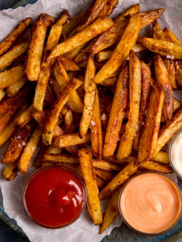 Chips on a plate on top of baking parchment. 3 dipping bowls of sauce on the plate.