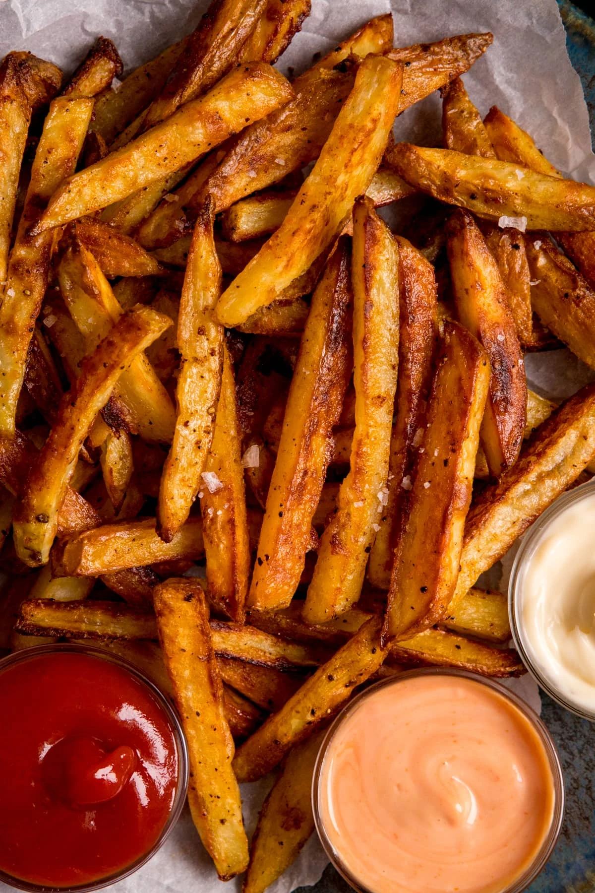 Close up overhead image of crispy oven fries with a selection of sauces on baking parchment.