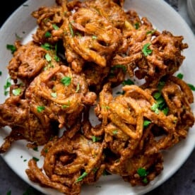 Onion bhajis on a white plate, sprinkled with coriander.