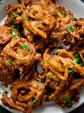 Onion bhajis on a white plate, sprinkled with coriander.