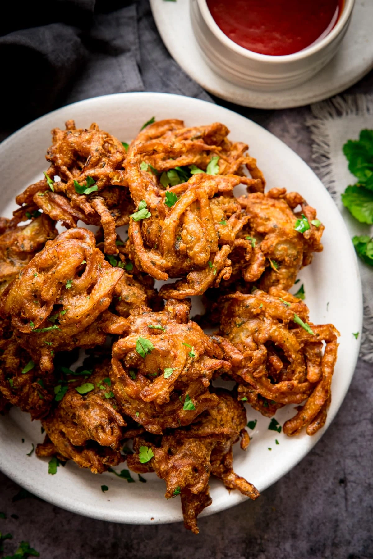 Onion bhajis on a white plate. Small white bowl filled with chilli sauce just in shot.