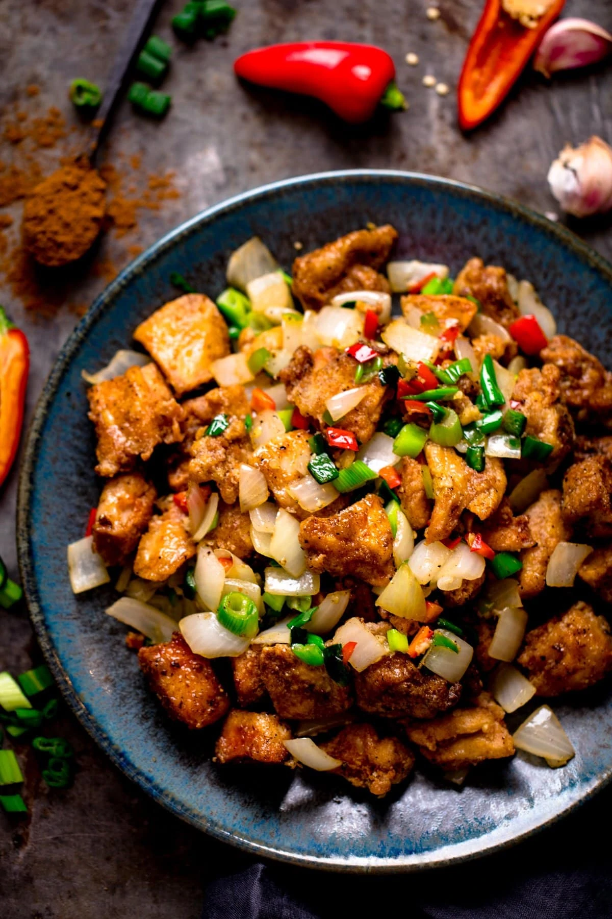 salt and pepper chicken on a dark blue plate with ingredients scattered around the plate