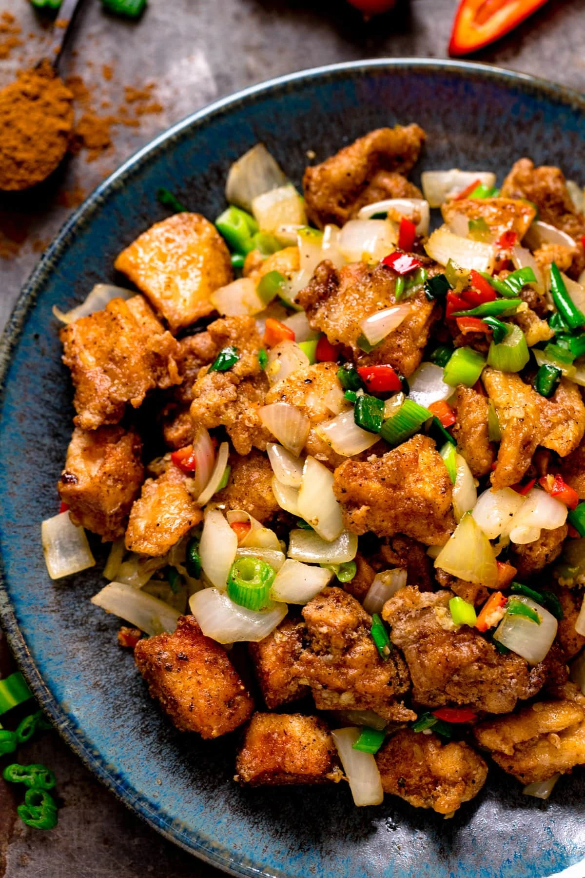 Close up overhead image of salt and pepper chicken on a dark blue plate