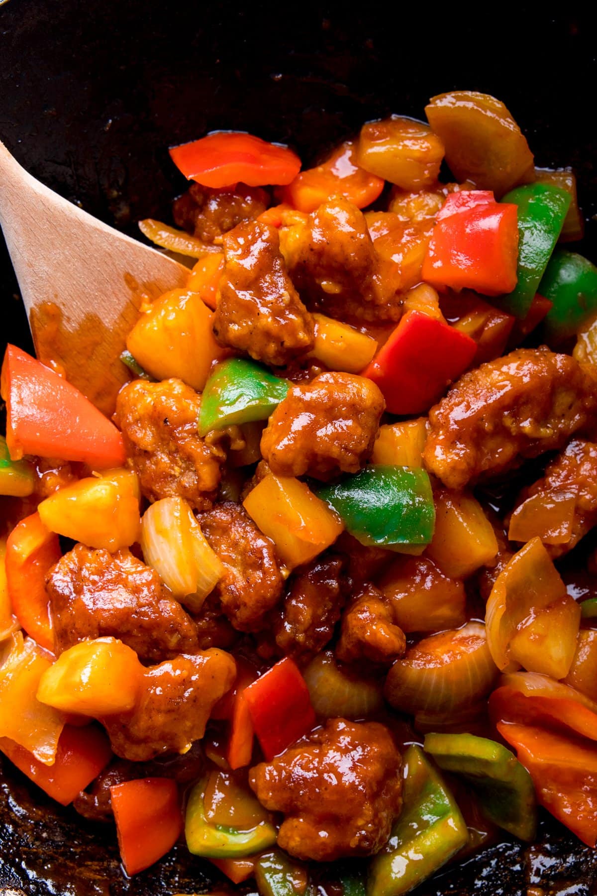 Close up of sweet and sour pork in a wok with peppers, onion and pineapple