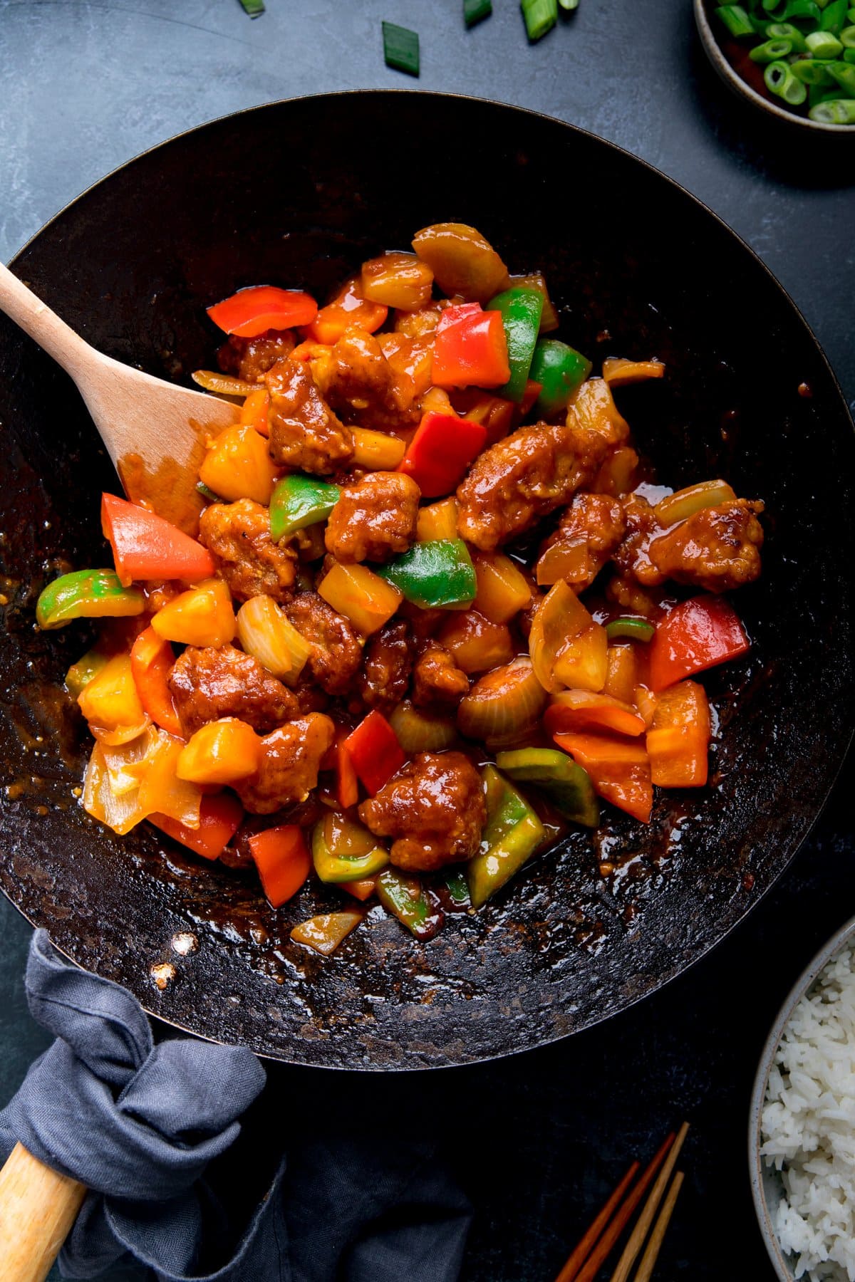 Overhead of sweet and sour pork in a wok on a blue surface