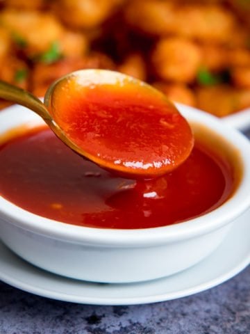 Spoonful of sweet and sour sauce being taken from a small white bowl of sauce.
