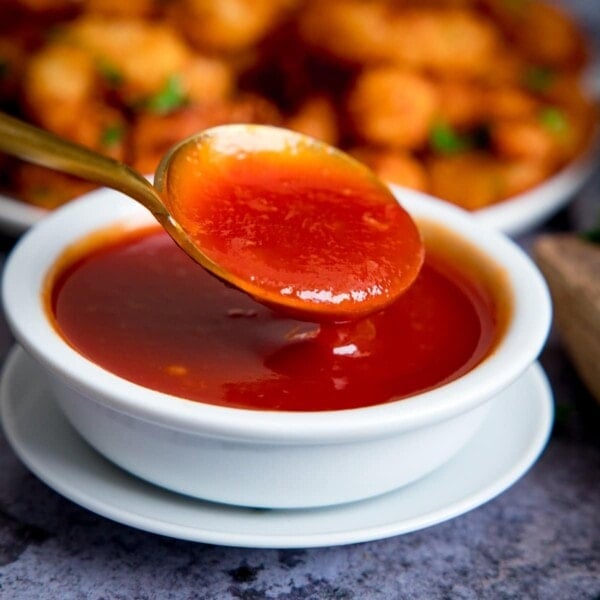 Spoonful of sweet and sour sauce being taken from a small white bowl of sauce.