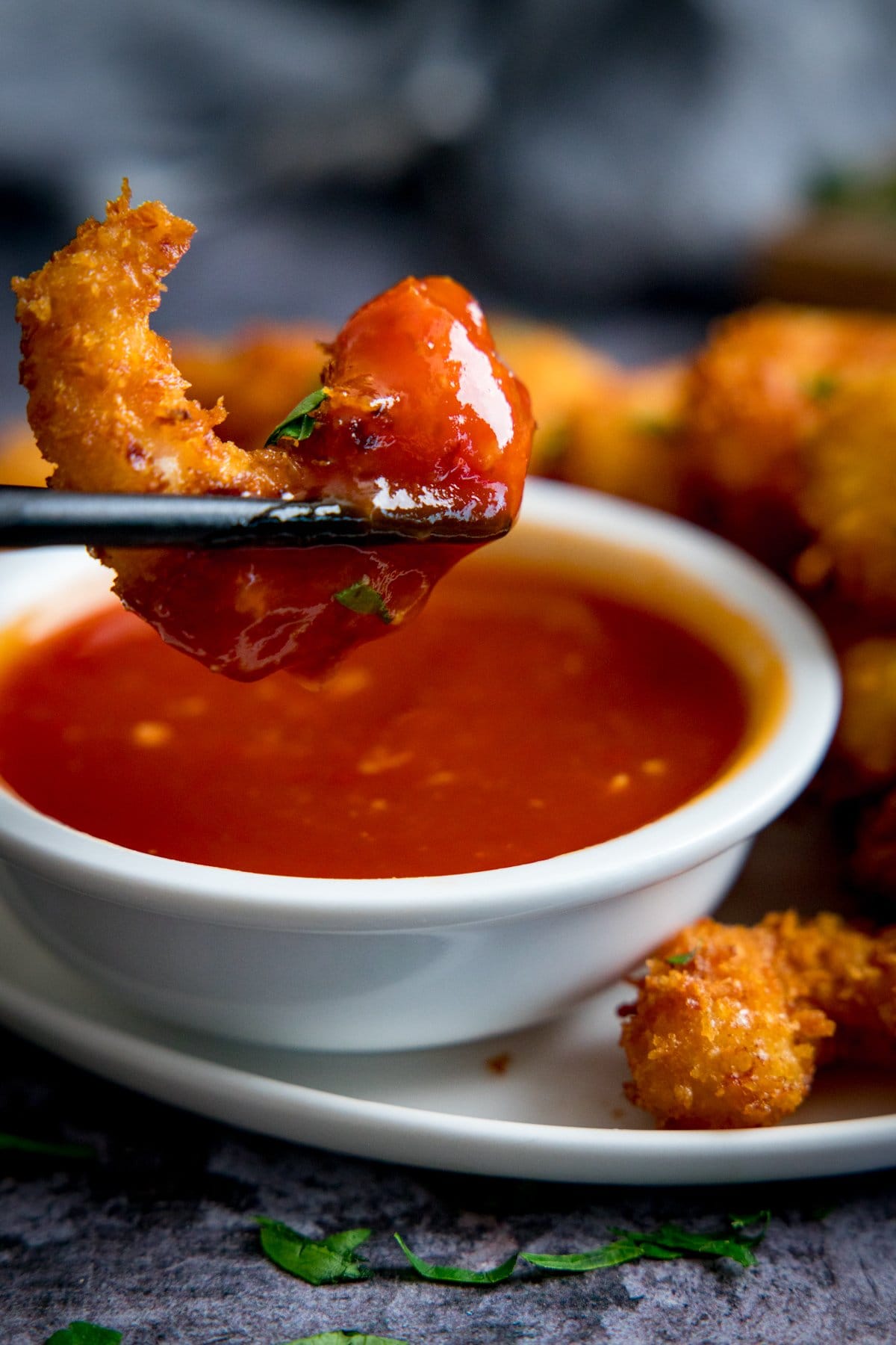 Coconut prawn being lifted out of a small bowl of sweet and sour sauce with chopsticks