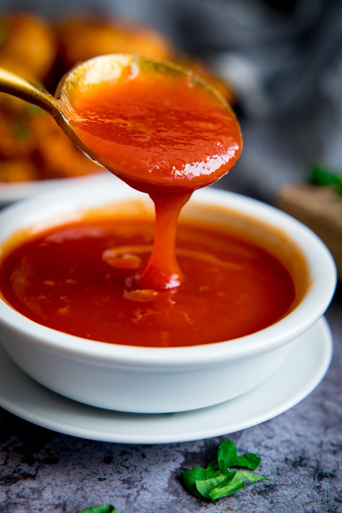 Spoonful of sweet and sour sauce being poured into a small white bowl of sweet and sour sauce