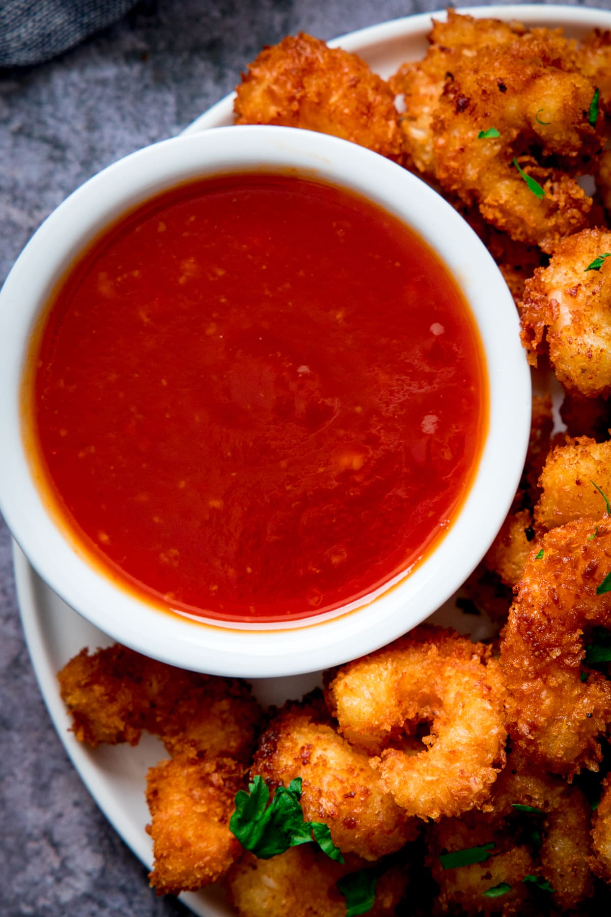 Small white bowl filled with sweet and sour sauce on a place with coconut prawns