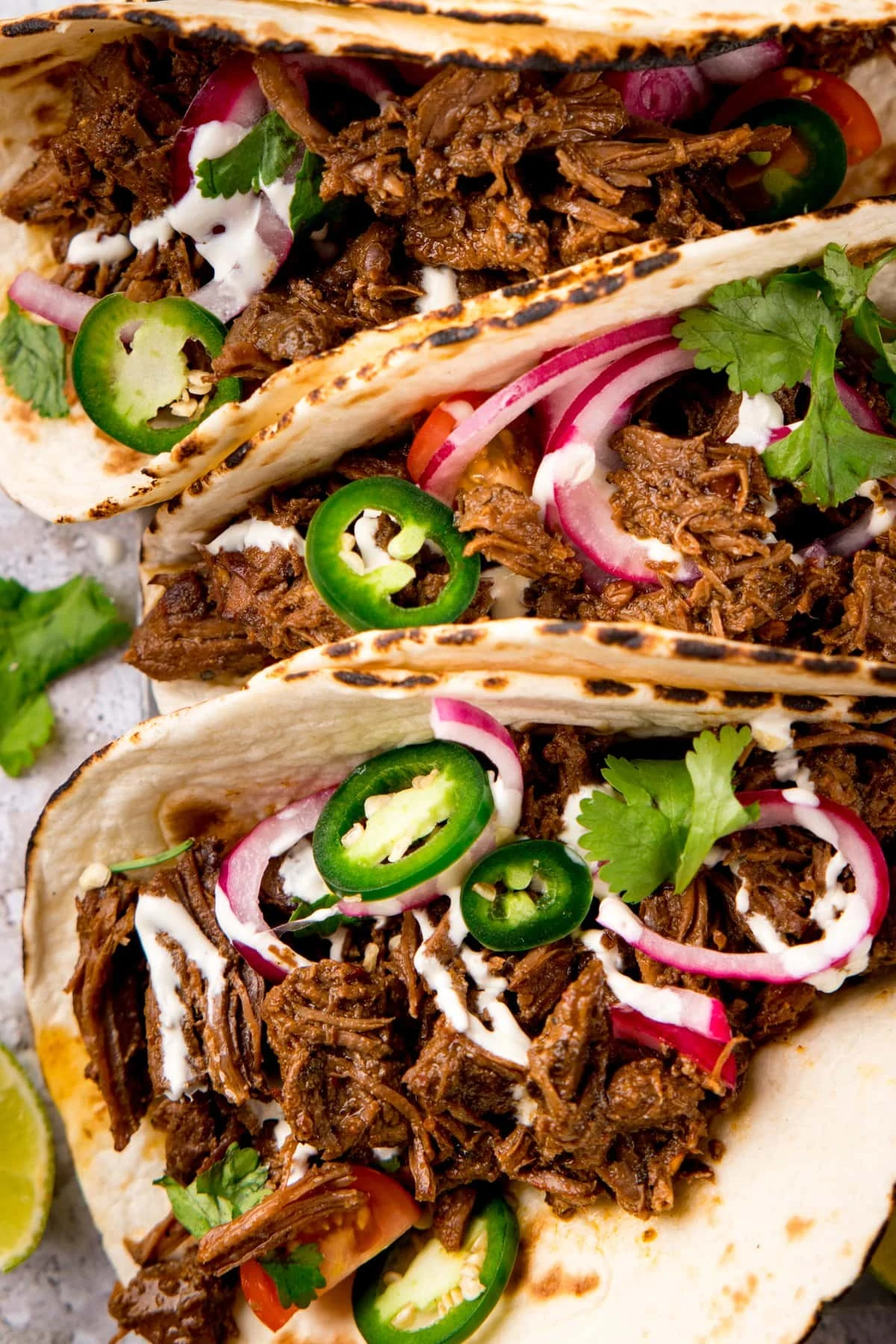 Close up overhead shot of beef barbacoa tacos topped with jalapeno and red onion slices