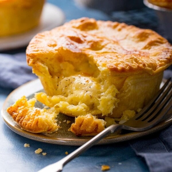 Square image of a small cheese and onion pie on a plate with a piece taken out.