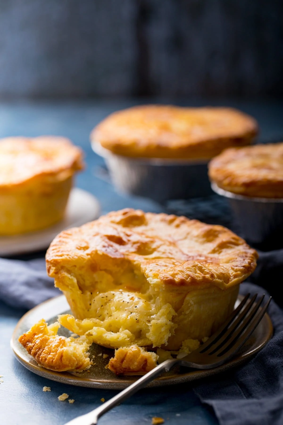 4 individual cheese and onion pies on a blue surface. Piece taken out of the pie at the front of the image.