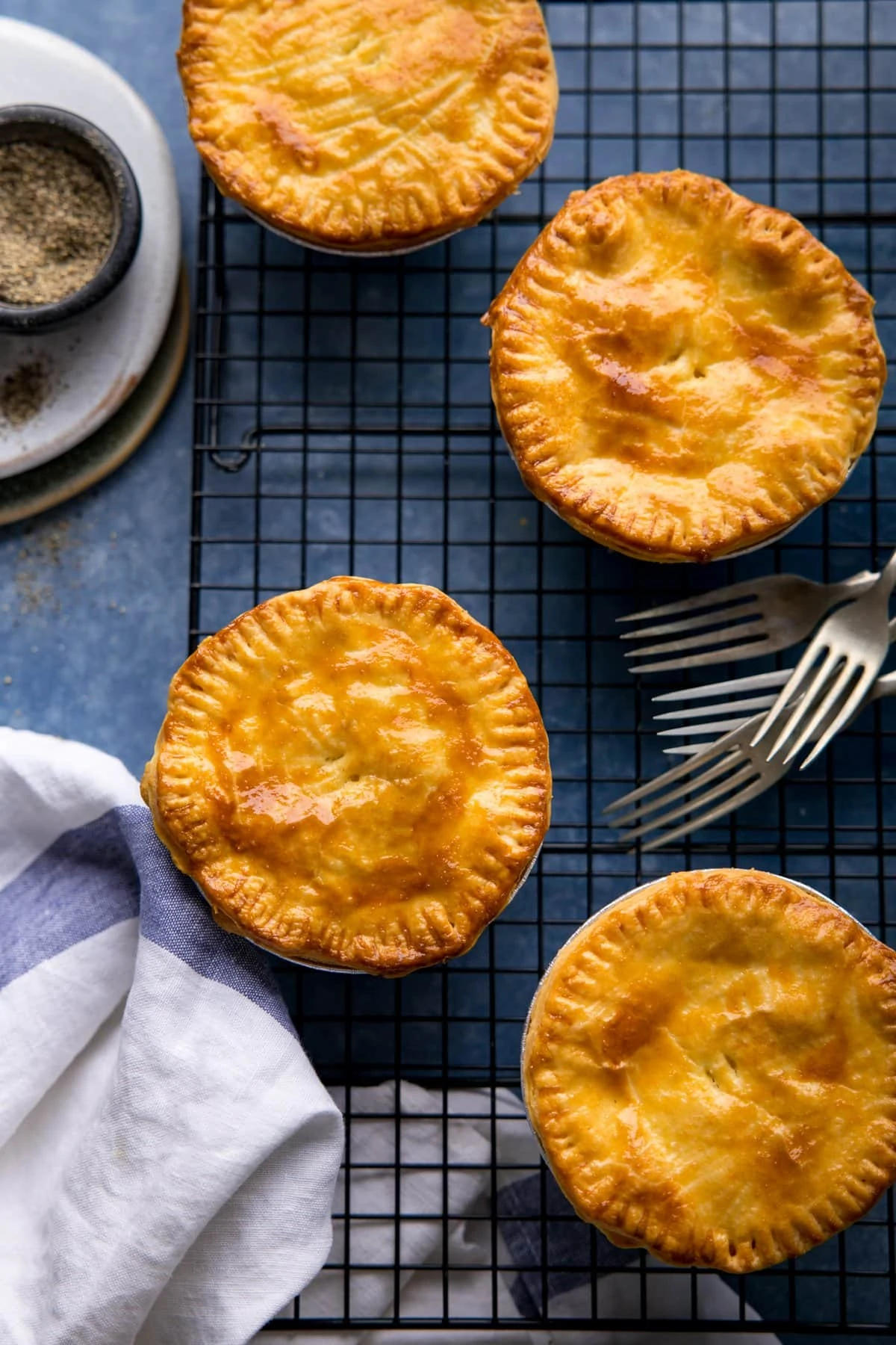 Overhead image of 4 cheese and onion pies on a cooling rack on a blue surface.