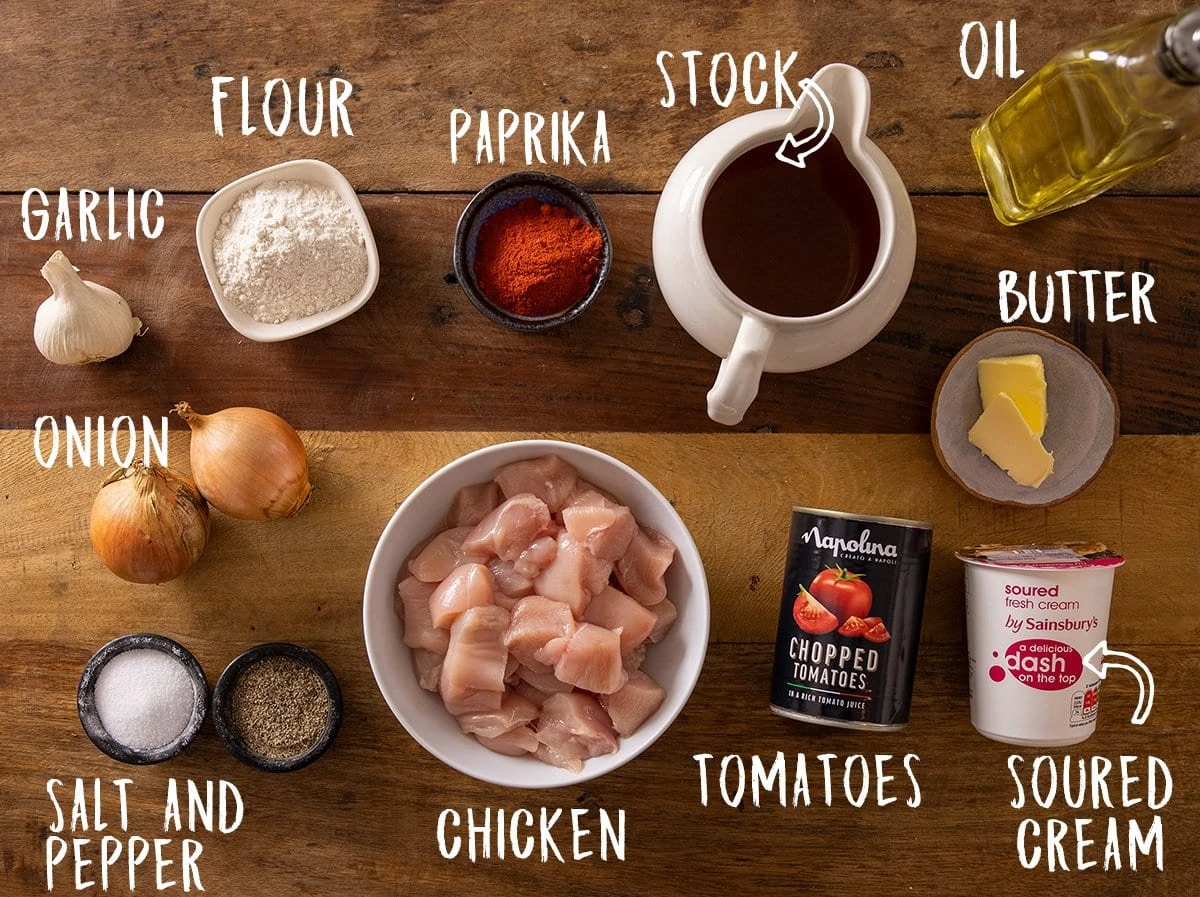 Ingredients for chicken paprikash on a wooden table.
