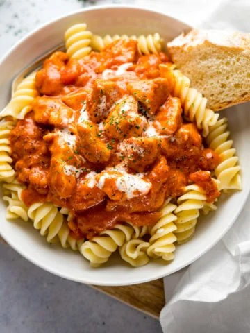 Chicken Paprikash in a white bowl on top of pasta with a piece of bread in the bowl.