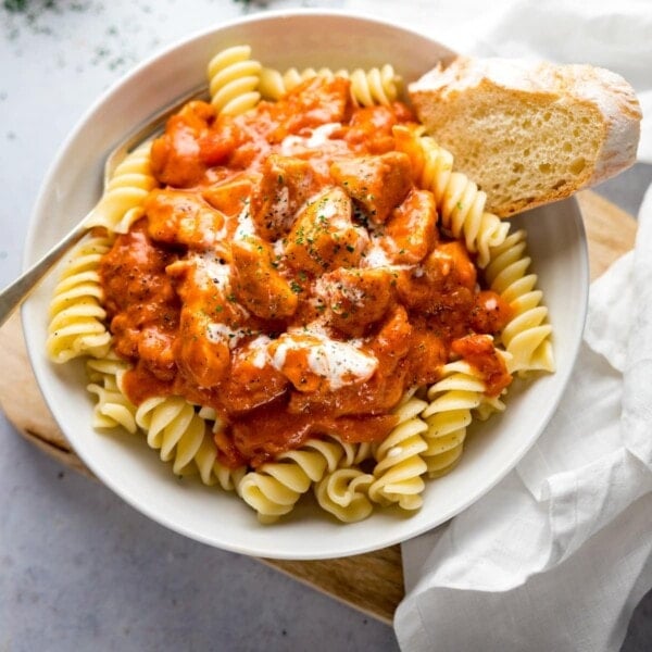 Chicken Paprikash in a white bowl on top of pasta with a piece of bread in the bowl.