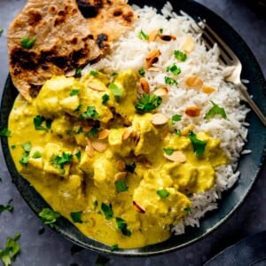 Chicken pasanda and rice on a dark plate with a piece of chapati on the plate.