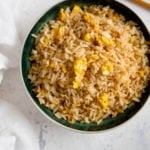 Egg fried rice on a dark bowl on a white background.