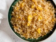 Egg fried rice on a dark bowl on a white background.