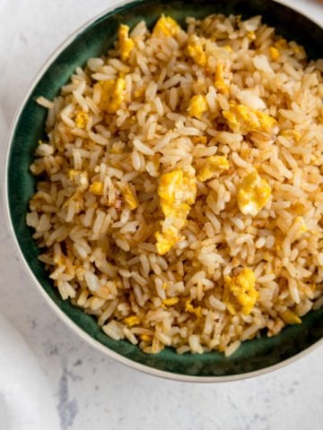 Egg fried rice on a dark bowl on a white background.