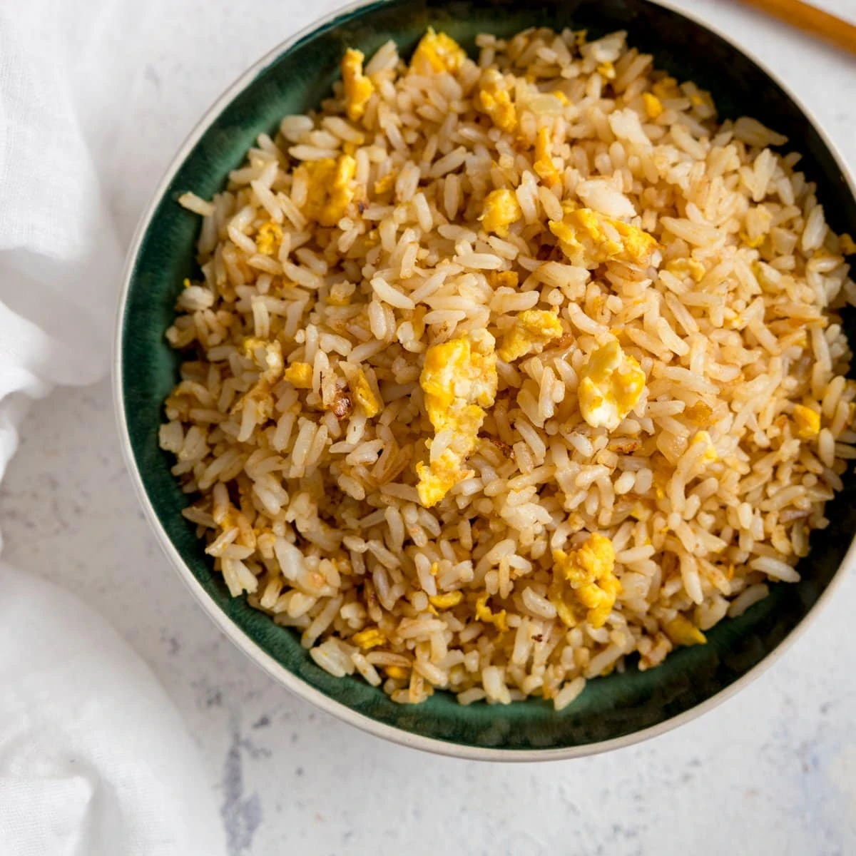 Egg fried rice on a dark bowl on a white background.