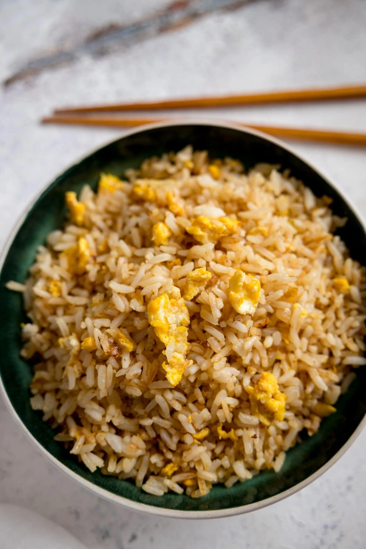 Egg fried rice in a dark bowl on a white background with wooden chopsticks.