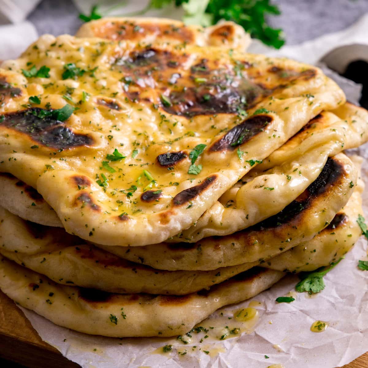 Pile of garlic naan breads on a piece of parchment on top of a wooden board.
