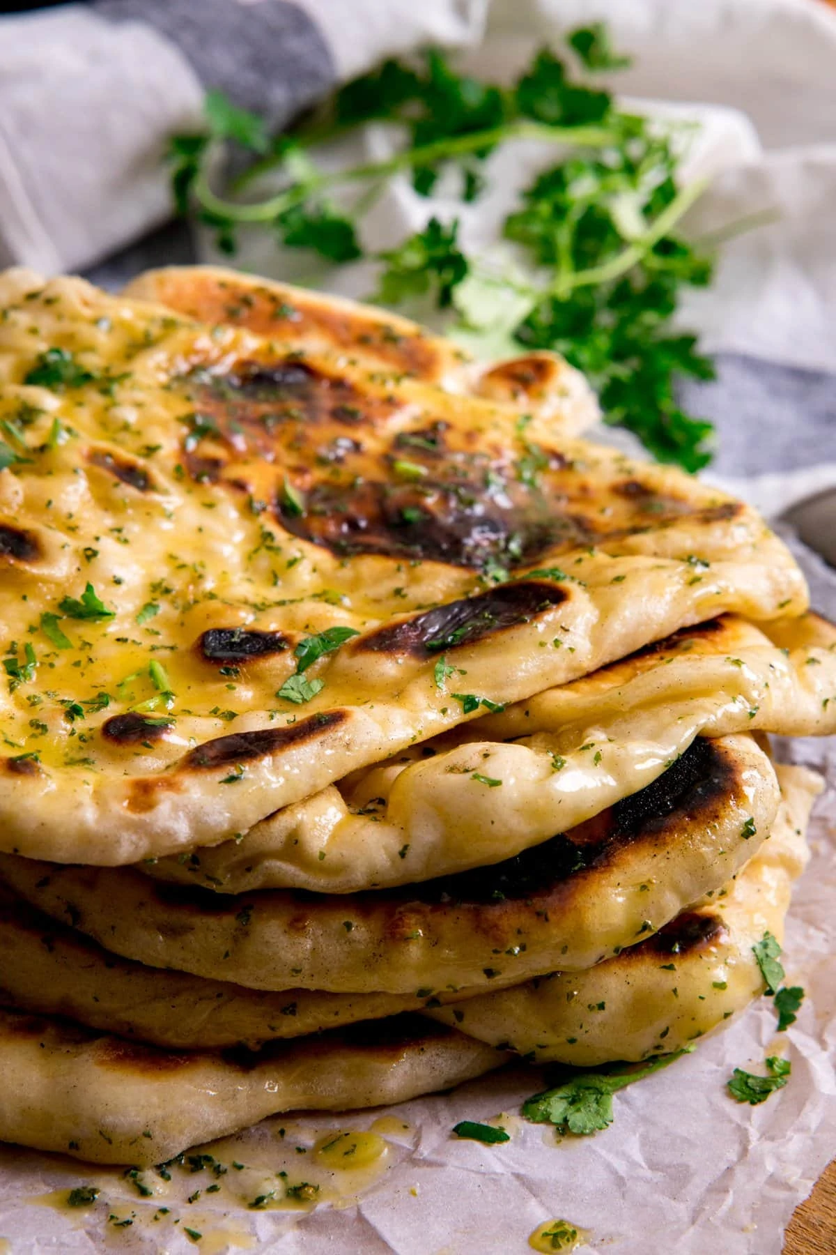 Pile of garlic naan breads on a piece of parchment paper.