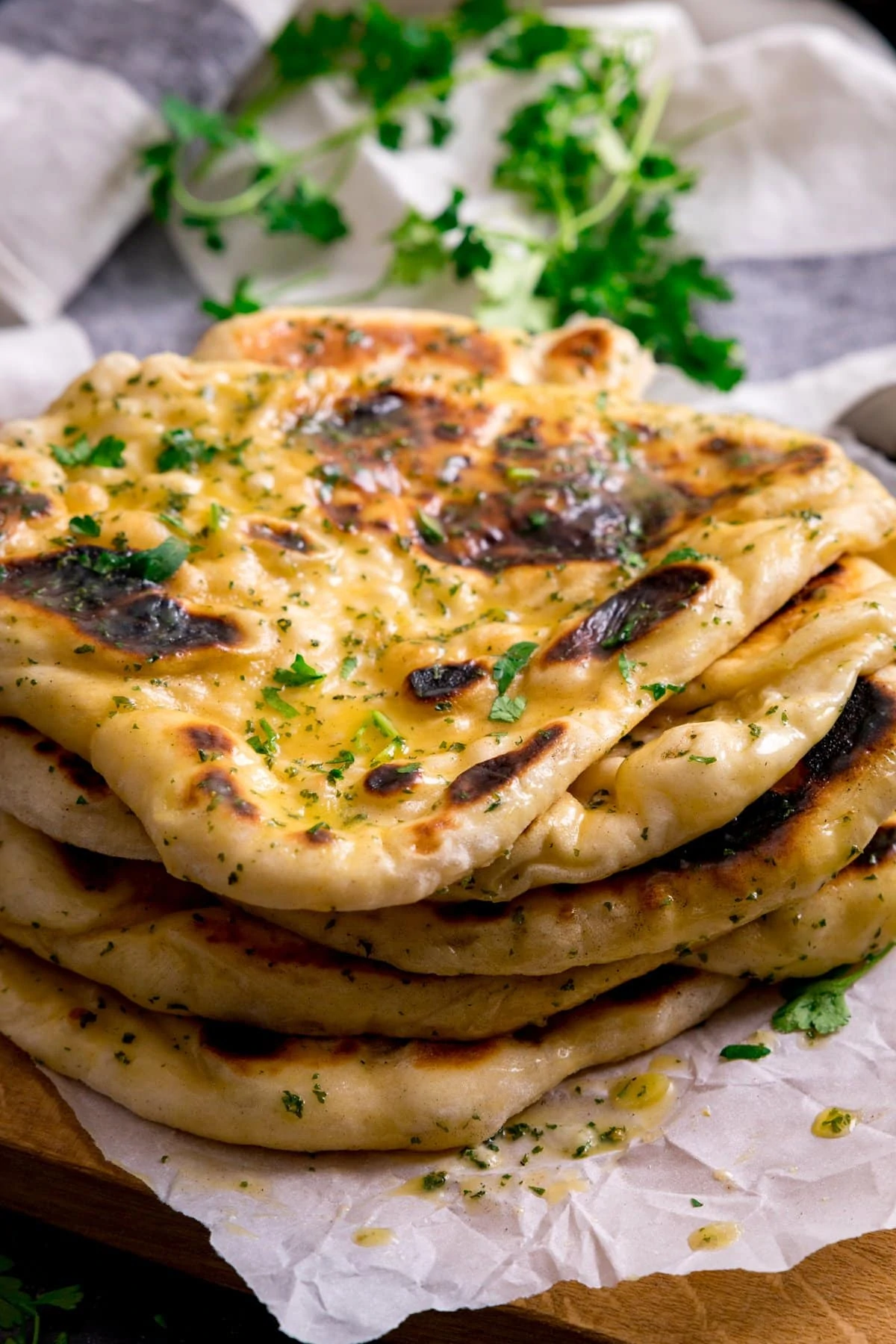 Pile of garlic naan breads on a light background. Fresh herbs in the background.