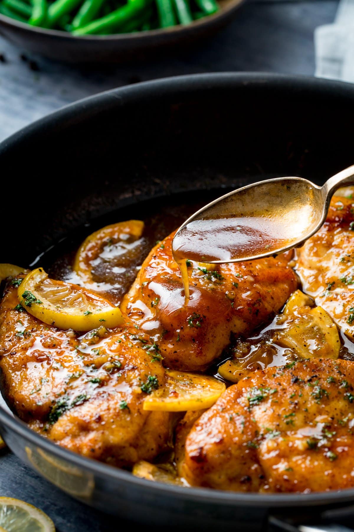 Sauce being spooned over chicken in a pan of honey lemon chicken.