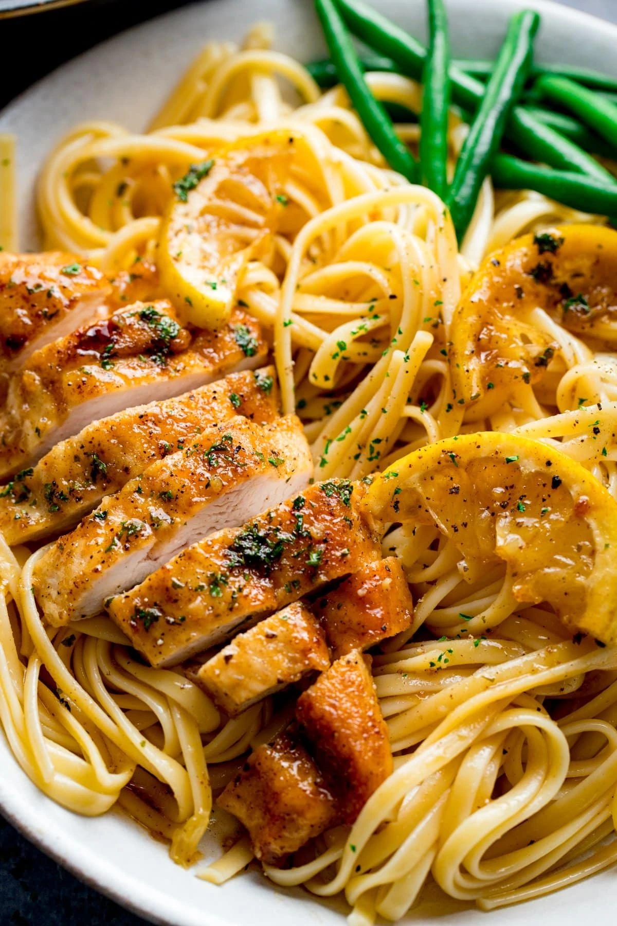 Sliced honey lemon chicken breast on a plate of linguine with green beans.