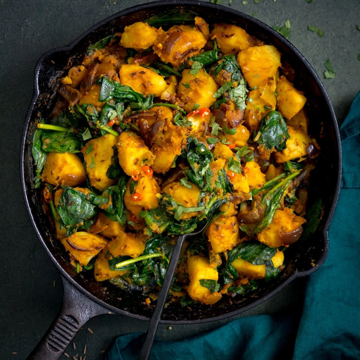 saag aloo in a black pan on a dark background