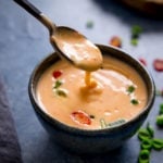 Spoonful of bang bang sauce being lifted from a bowl on a dark surface.