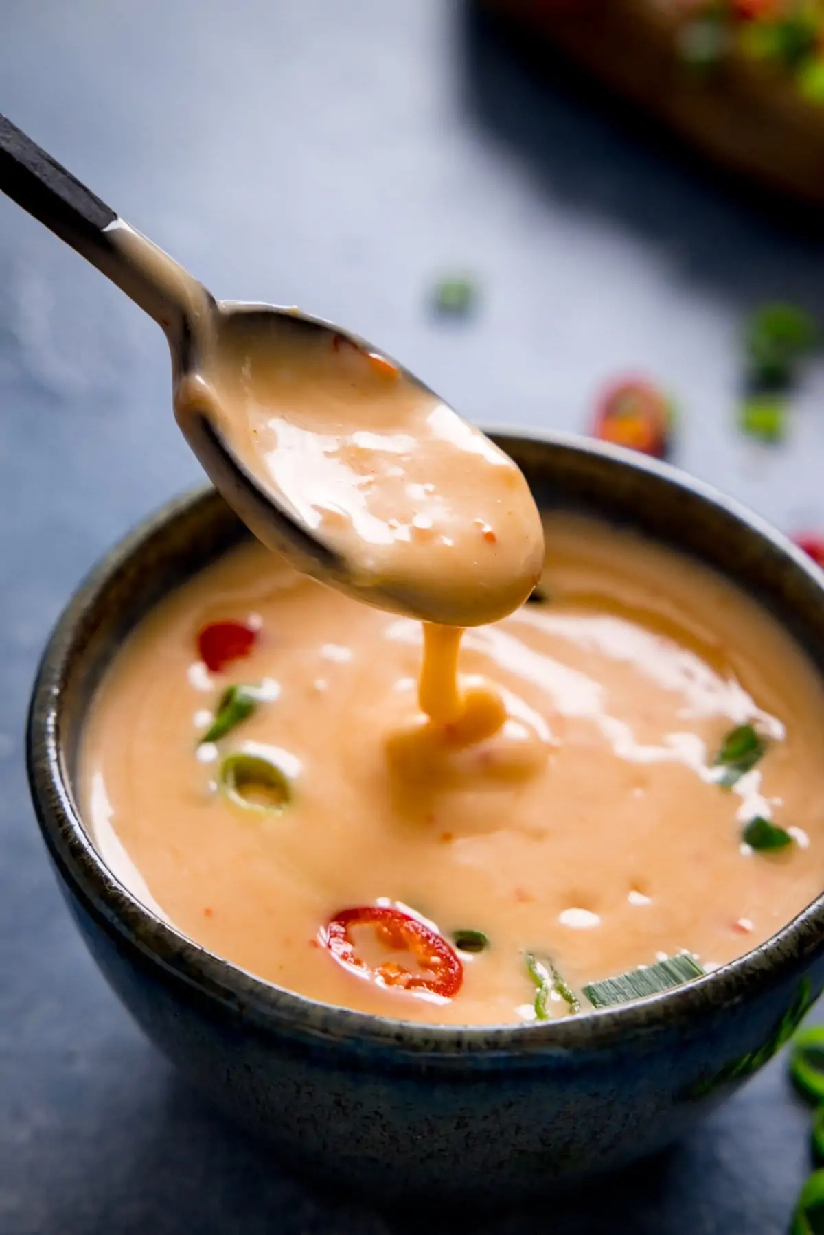 Spoonful of bang bang sauce being lifted from a small dark bowl.