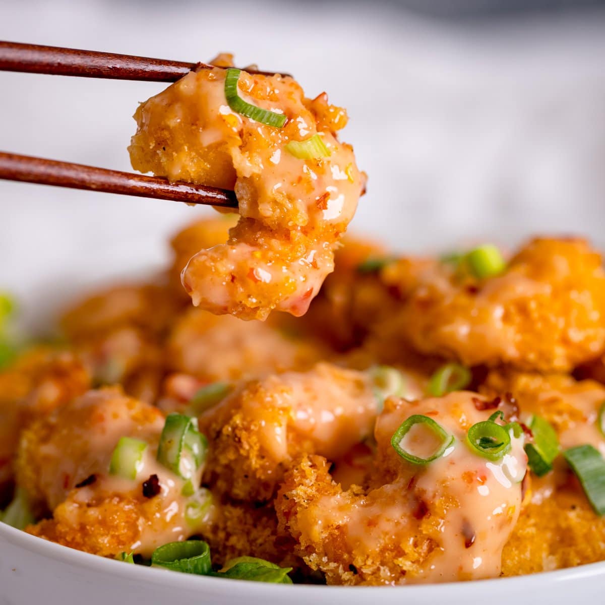 Crispy shrimp being lifted out of a bowl with chopsticks. Shrimp is covered with bang bang sauce.