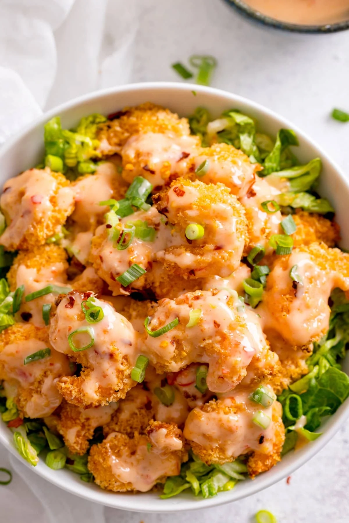 Overhead image of a white bowl filled with lettuce, crispy prawns and drizzled with bang bang sauce.