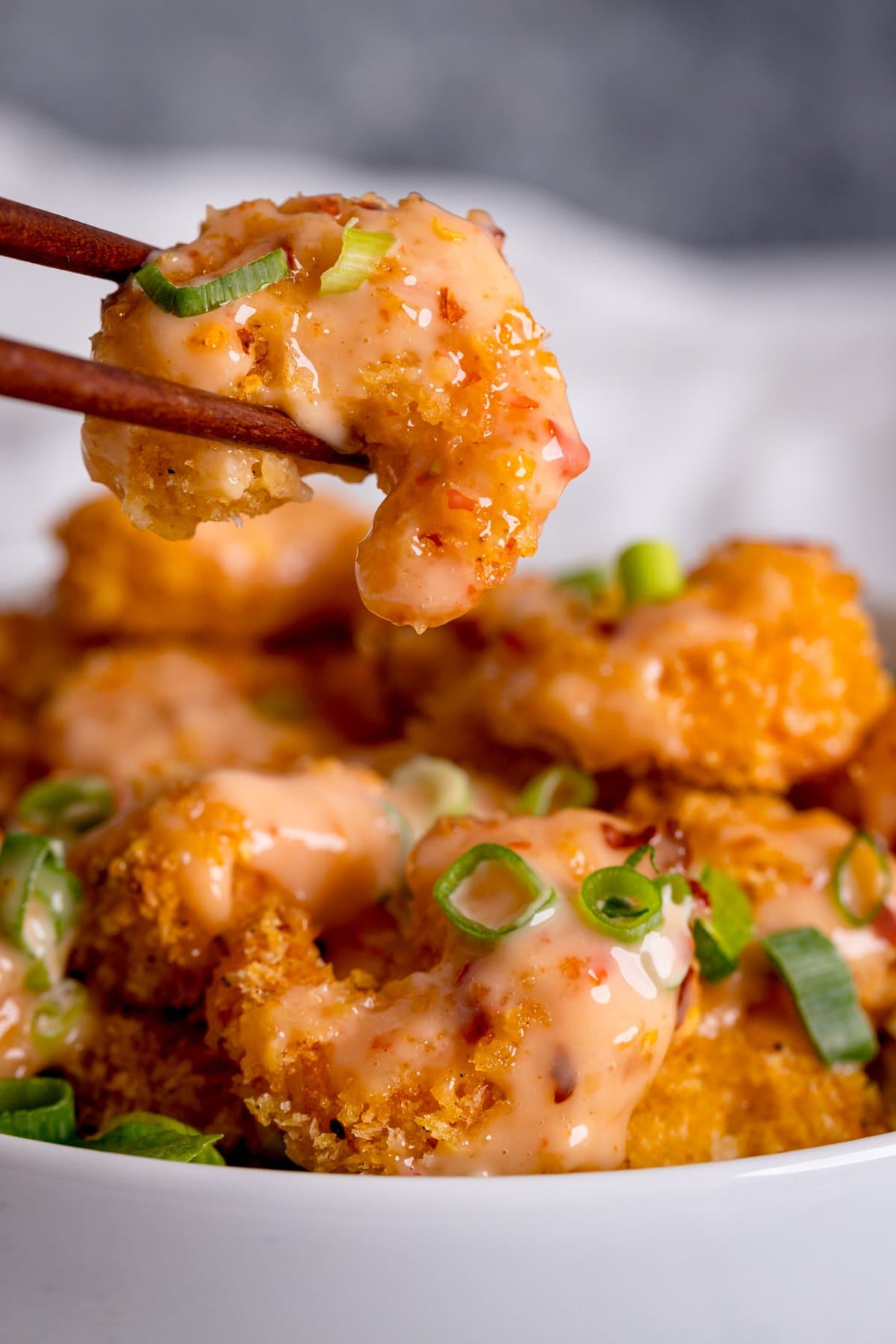 Crispy shrimp in bang bang sauce being lifted from a bowl with chopsticks.
