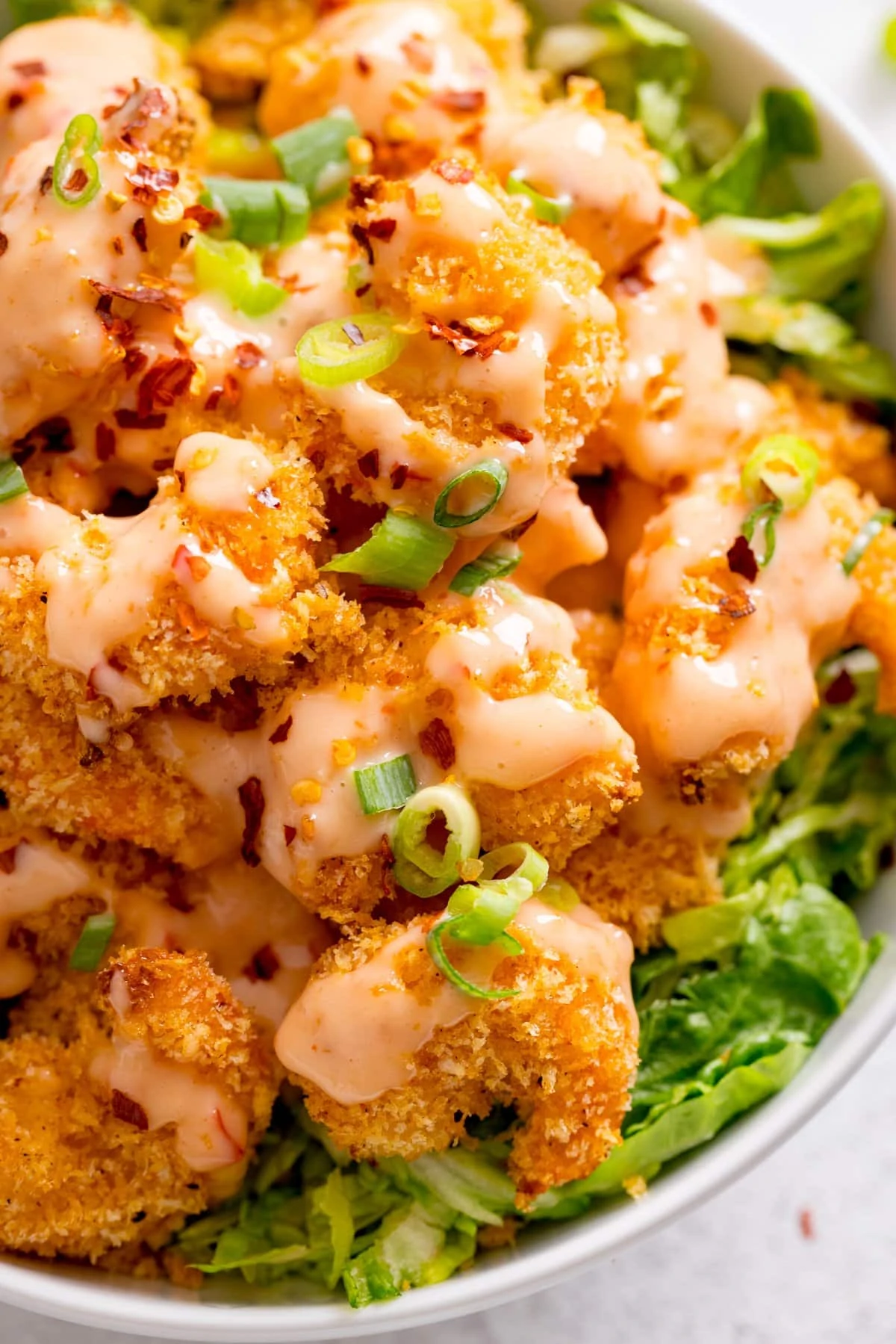 White bowl filled with lettuce and crispy prawns, topped with bang bang sauce.